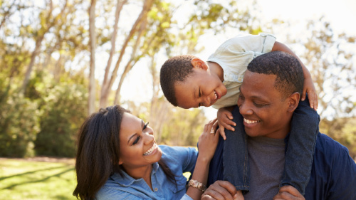 Parents Carrying Son On Shoulders As They Walk In Park