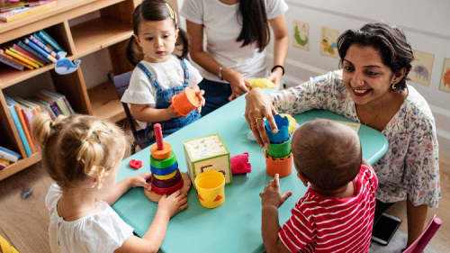 Nursery age children playing with daycare provider in the classroom